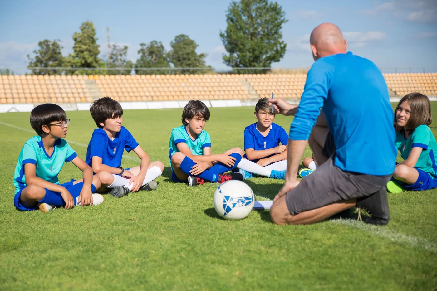 Coach talking with a group of young players sitting on the pitch