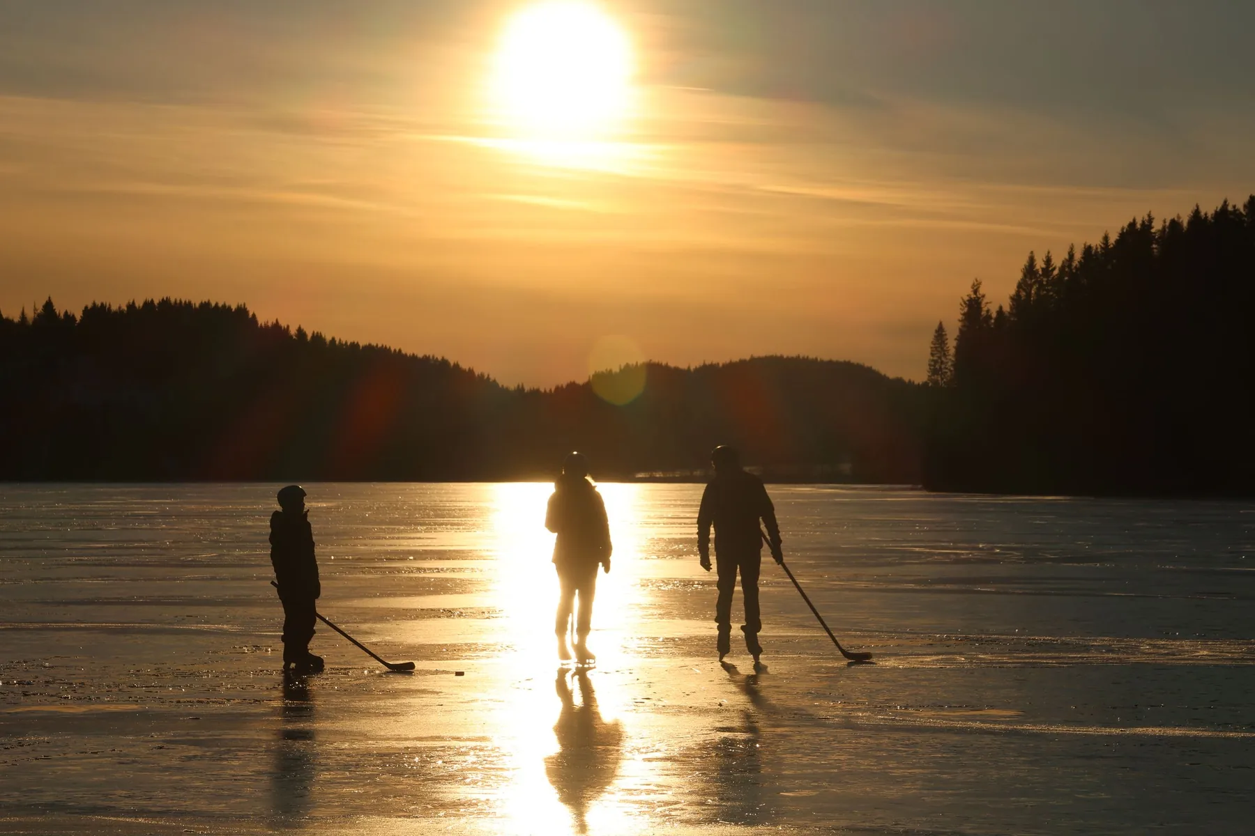 Players skating on a frozen pond at sunset