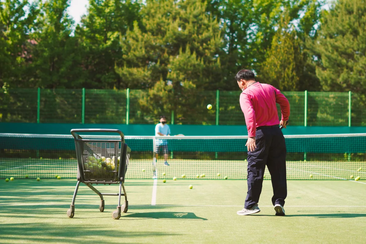 Tennis coach feeding balls to a junior player